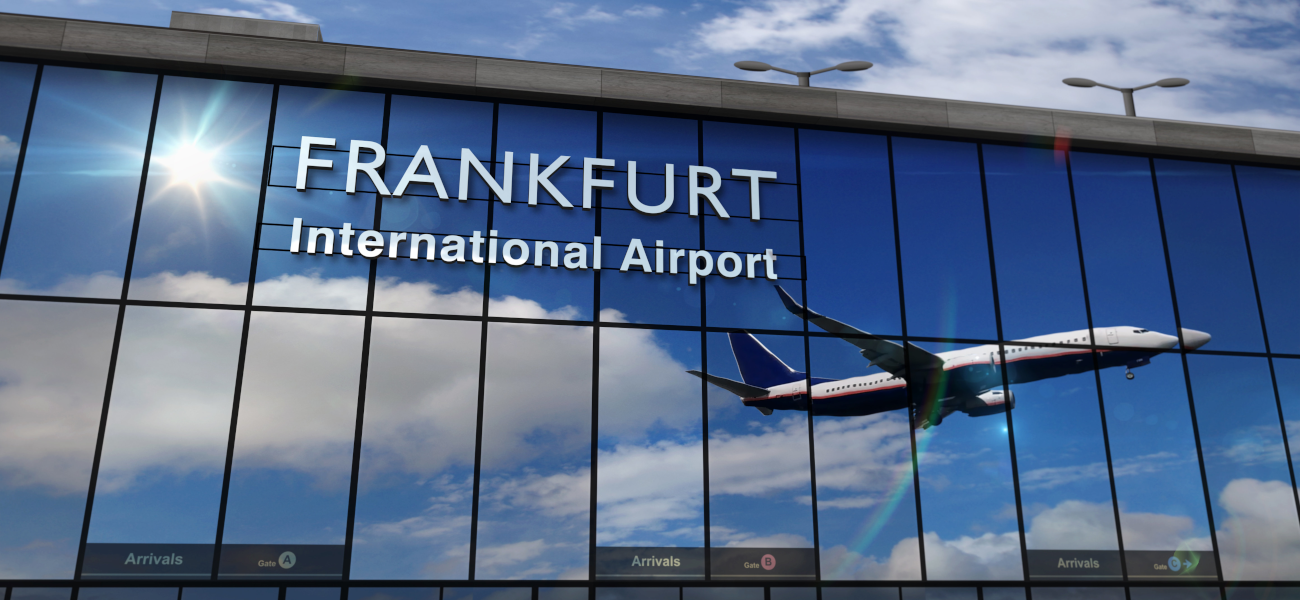 Foto startendes Flugzeug, das sich im Schaufenster einer großen Halle mit der Aufschrift "Frankfurt INernational Airport" spiegelt.