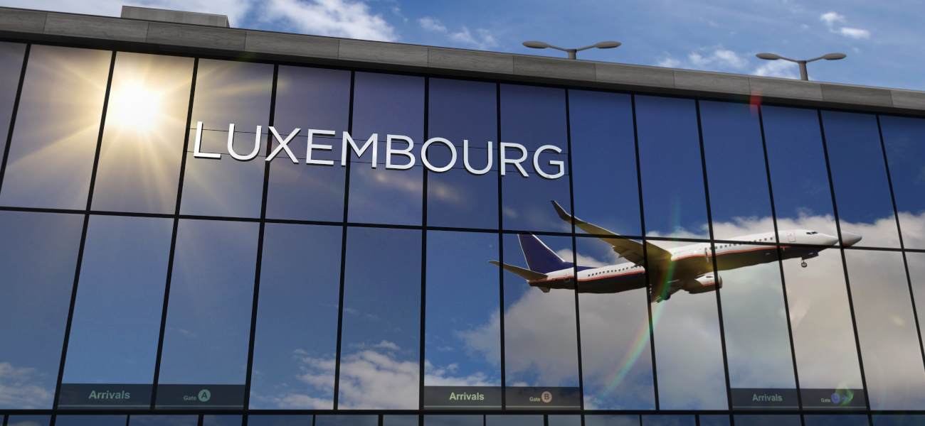 Foto startendes Flugzeug, das sich im Schaufenster einer großen Halle mit der Aufschrift "Luxembourg" spiegelt.